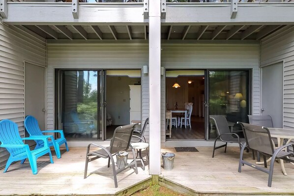 Un patio techado con mobiliario exterior, incluyendo sillas de plástico azul y sillas de metal, y una zona de comedor con mesa y sillas.