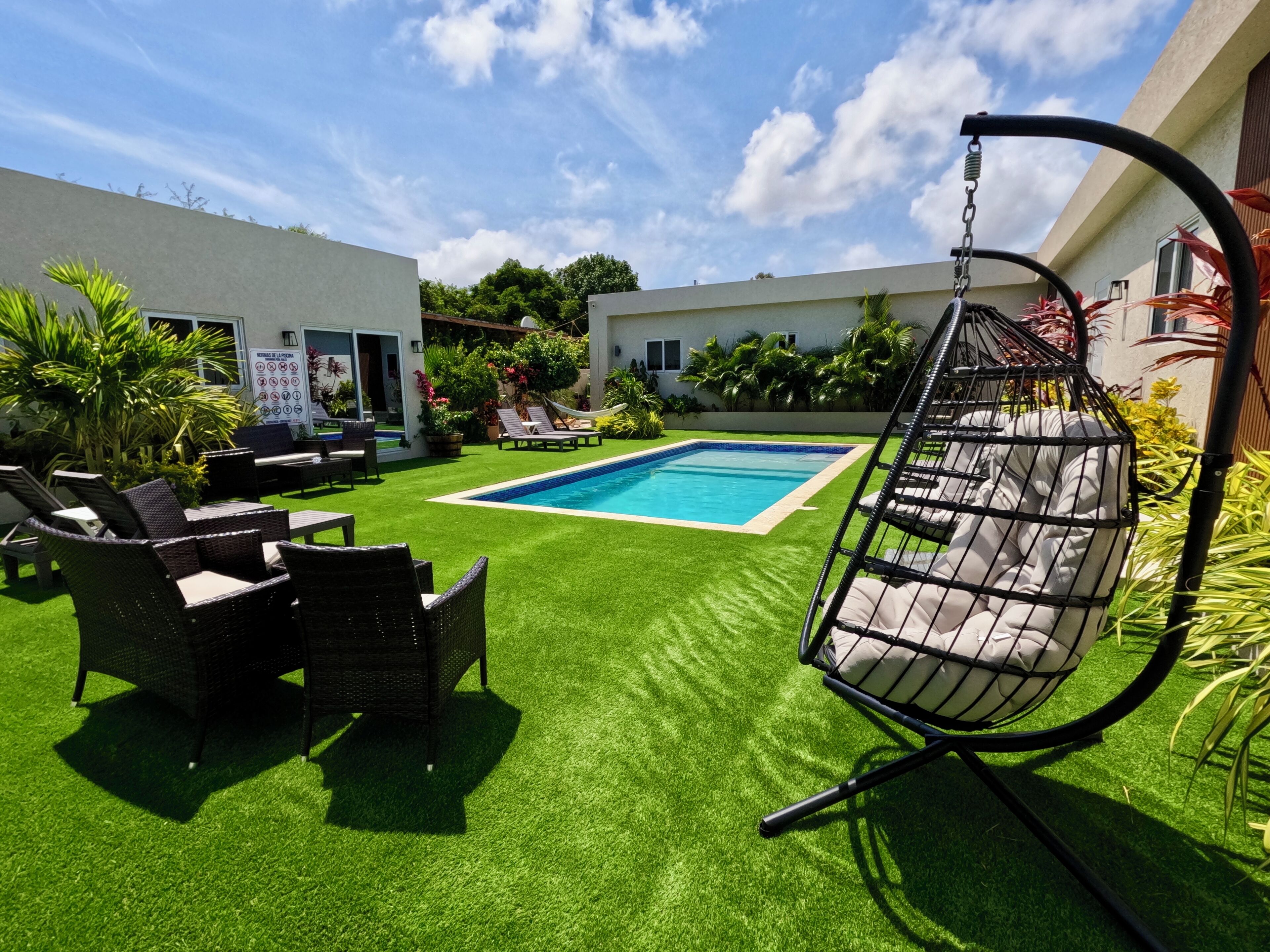 Ein Garten mit Schwimmbad, Rasen aus Kunstgrün, Gartenmöbeln und einer Hängematte.
