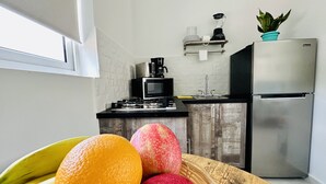 Cucina con forno a microonde, fornello, lavello e frigorifero. In primo piano, una ciotola di frutta con arance e mele.