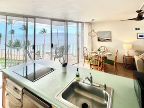 A kitchen with a view of the ocean, a dining area with chairs and a table, and a ceiling fan.