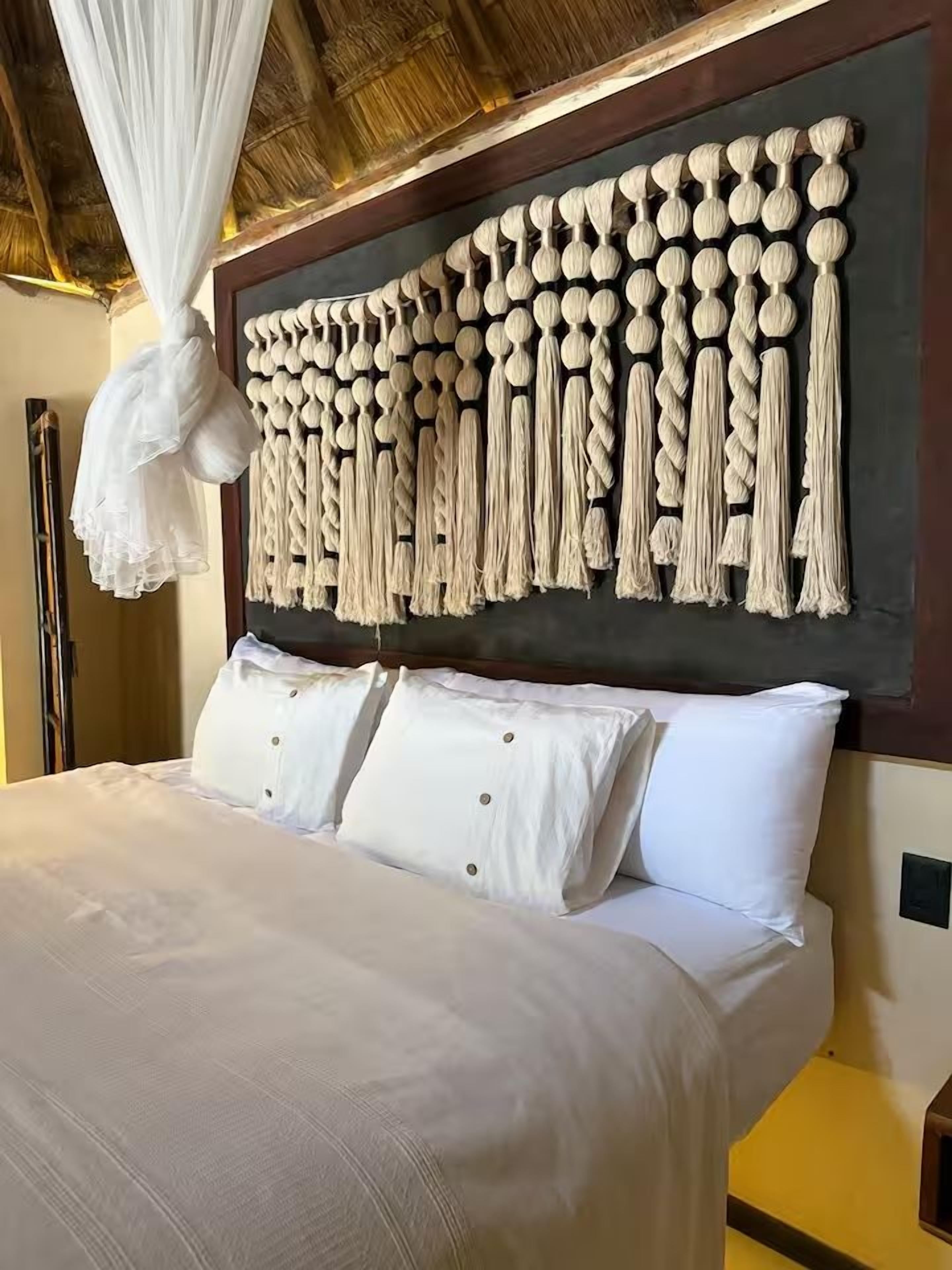 A bed with white bedding and a macramé wall hanging above it.