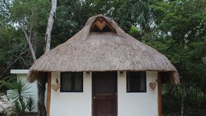 A thatched-roof hut with a wooden door and windows, surrounded by greenery. - Ka'ax Cenote Resort (Akumal)