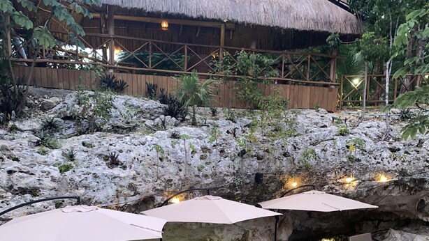 A wooden deck with wicker furniture and umbrellas, surrounded by a natural rock garden and a thatched-roof structure. - Ka'ax Cenote Resort (Akumal)