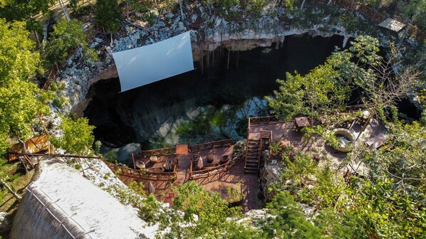 A cliffside view of a natural cave with a wooden deck and seating area overlooking the cave entrance. - Ka'ax Cenote Resort (Akumal)