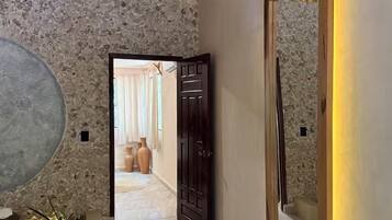 Un pasillo con pared de piedra, un espejo grande y una puerta de madera que da a otra habitación.