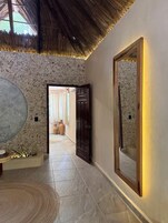 Un pasillo con pared de piedra, un espejo grande y una puerta de madera que da a otra habitación.