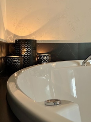 Um banheiro moderno com uma banheira grande e curvada, uma torneira elegante e arandelas decorativas na parede.