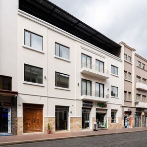 En bygning med flere etager, en flad facade, store vinduer og en hoveddør i træ i stueetagen.