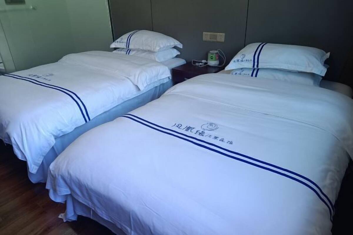 A hotel room with two beds, each with white bedding and a blue stripe. There is a nightstand with a lamp and a bottle of water.