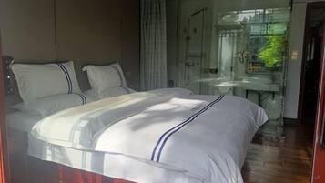 Una habitación de hotel moderna con una cama grande, cabina de ducha de vidrio y vistas a la ciudad.