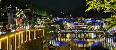 Vista nocturna de una zona junto al río con edificios iluminados y un puente.