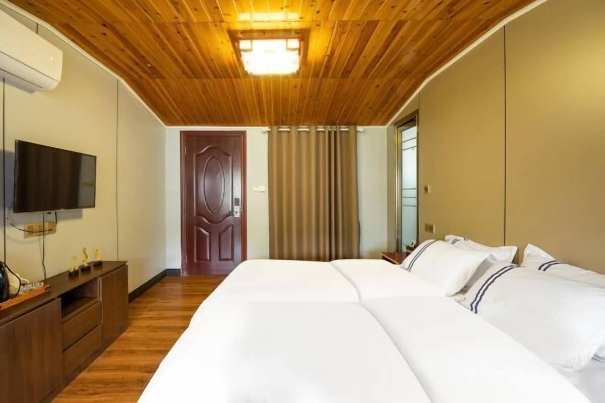 A hotel room with a wooden ceiling, a flat-screen TV, a bed with white linens, a wooden dresser, and a door leading to another room.