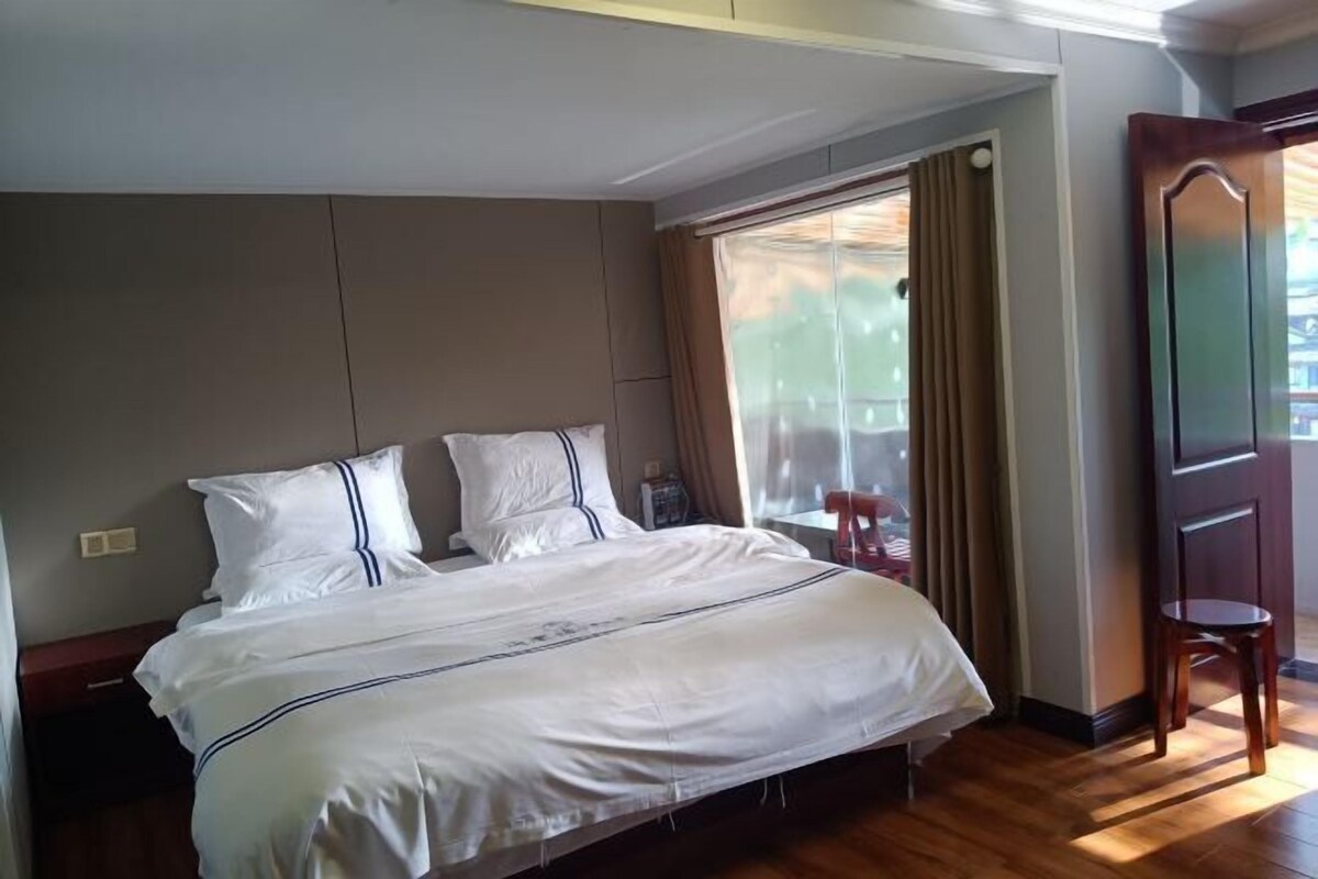 Habitación de hotel con una cama grande, piso de madera, una ventana con cortinas y una puerta.