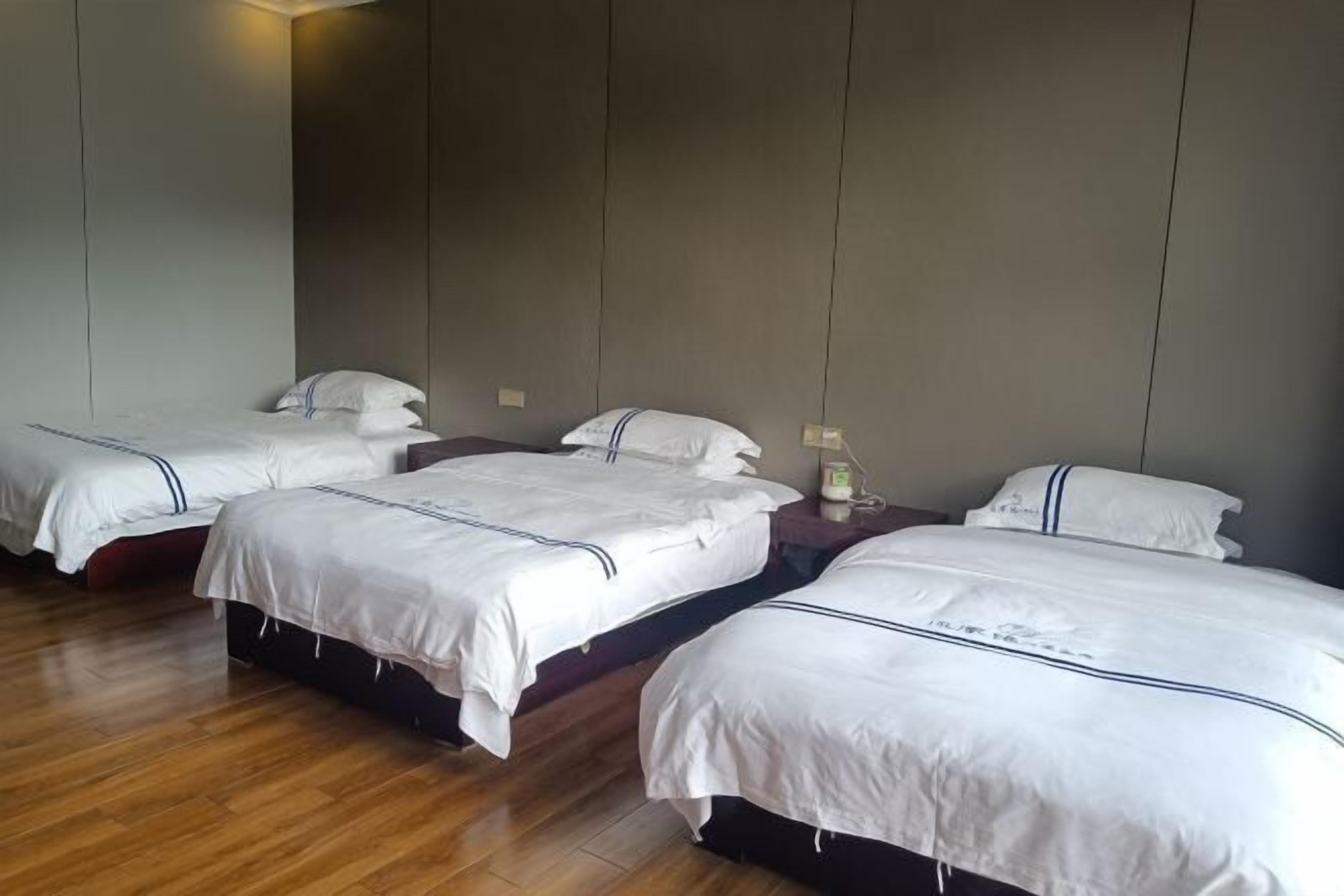 Habitación de hotel con cuatro camas individuales, cada una con ropa blanca y cabeceros oscuros. El suelo es de madera y las paredes son de un tono neutro.