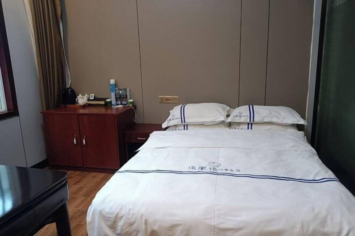 A hotel room with a bed, a wooden nightstand, a desk, and a wardrobe.