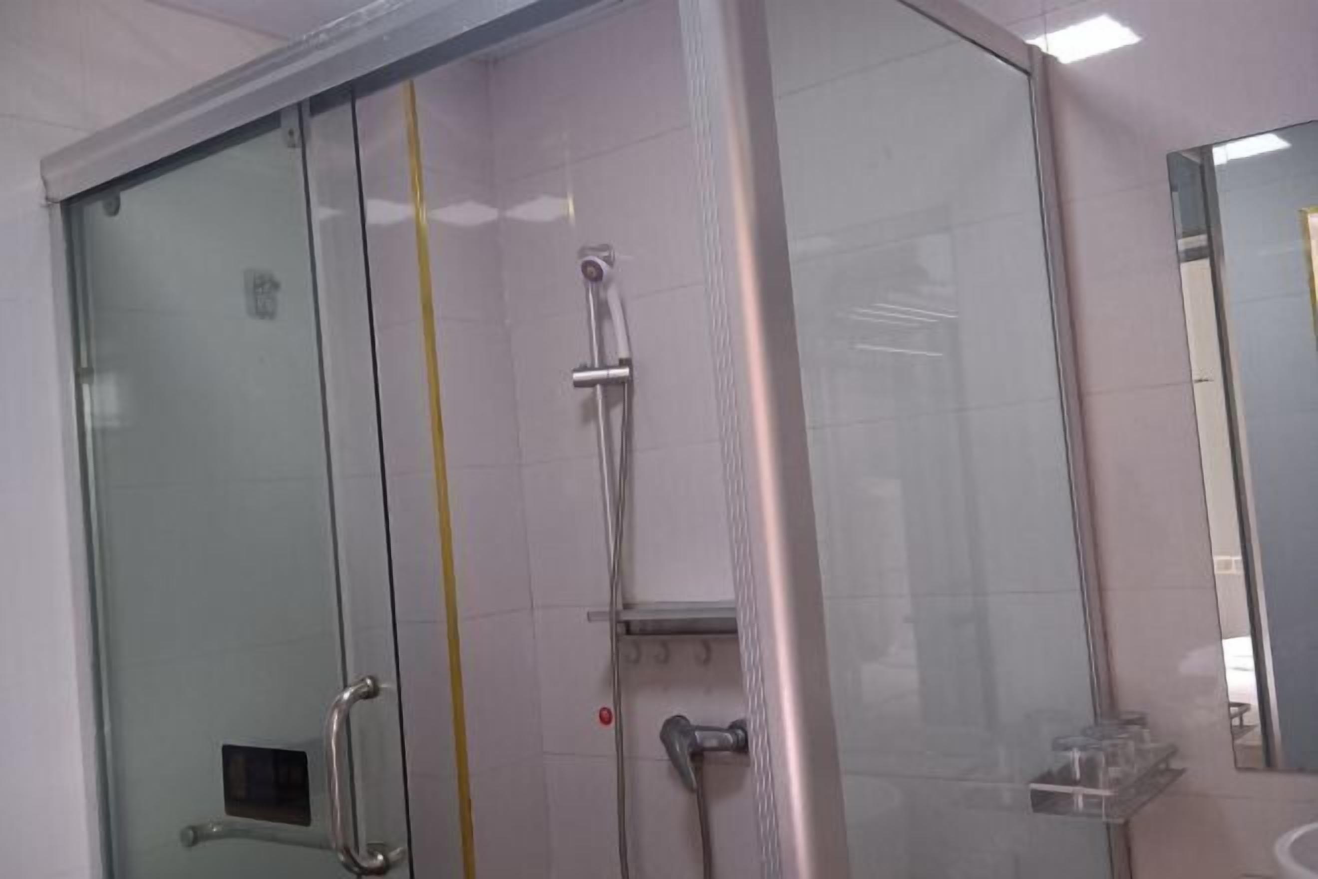 Ducha envuelta en vidrio con cabezal de ducha manual, puerta de cristal con manija y espejo en la pared contigua.