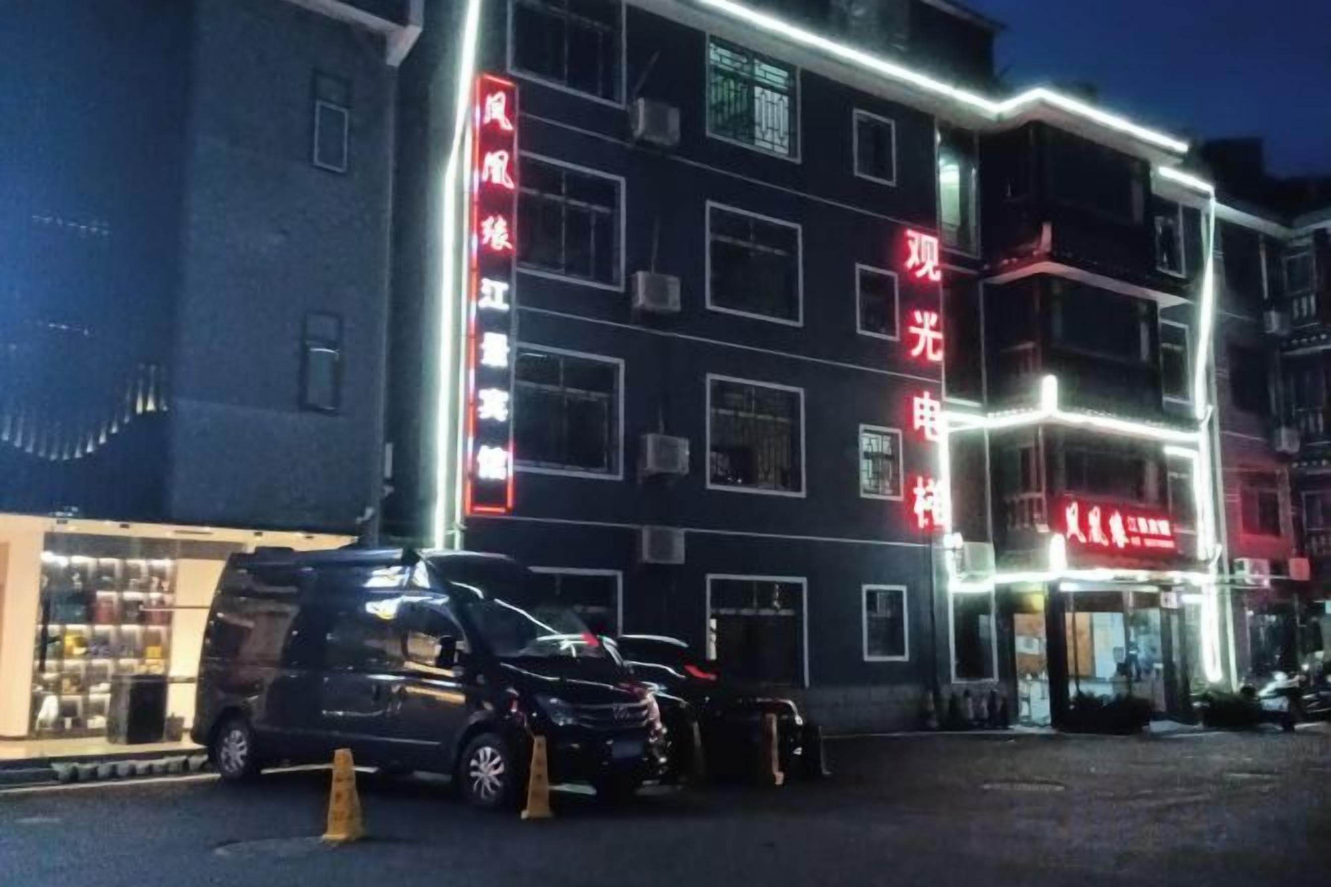 A multi-story building with illuminated signage, a parked car, and a visible storefront.
