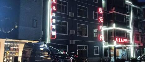 A multi-story building with illuminated signage, a parked car, and a visible storefront.