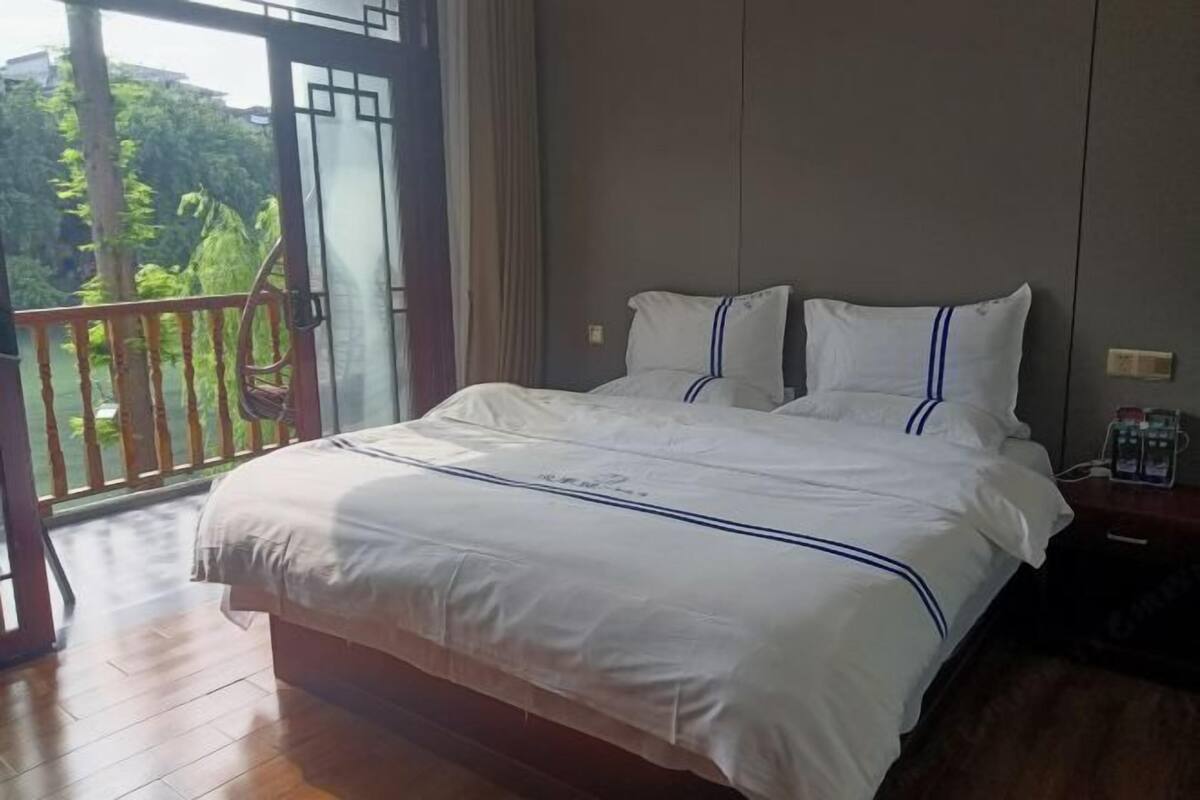 A bedroom with a bed, a nightstand, and a view of greenery through a balcony door.