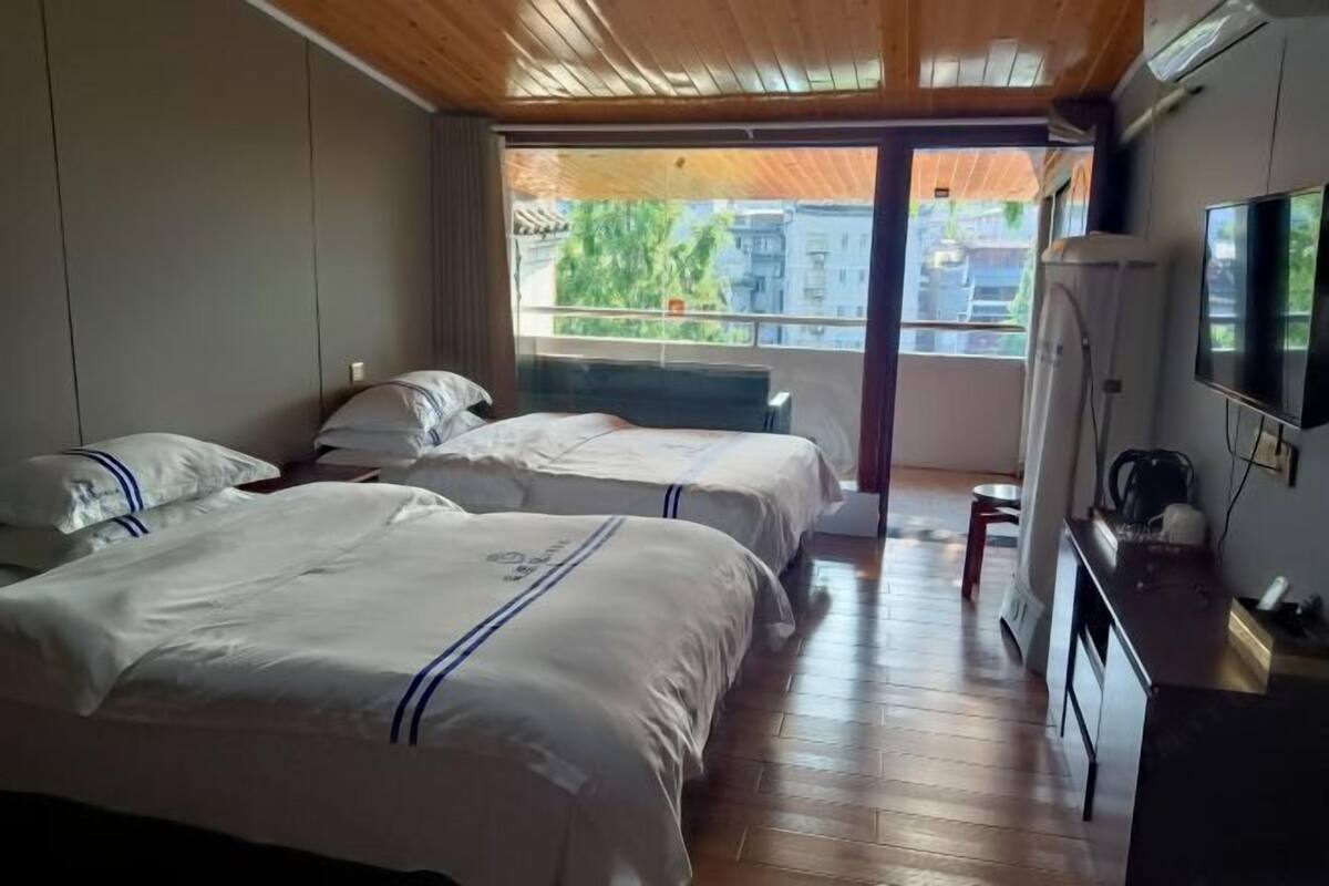A bedroom with two beds, a balcony, a TV, and a kitchenette.