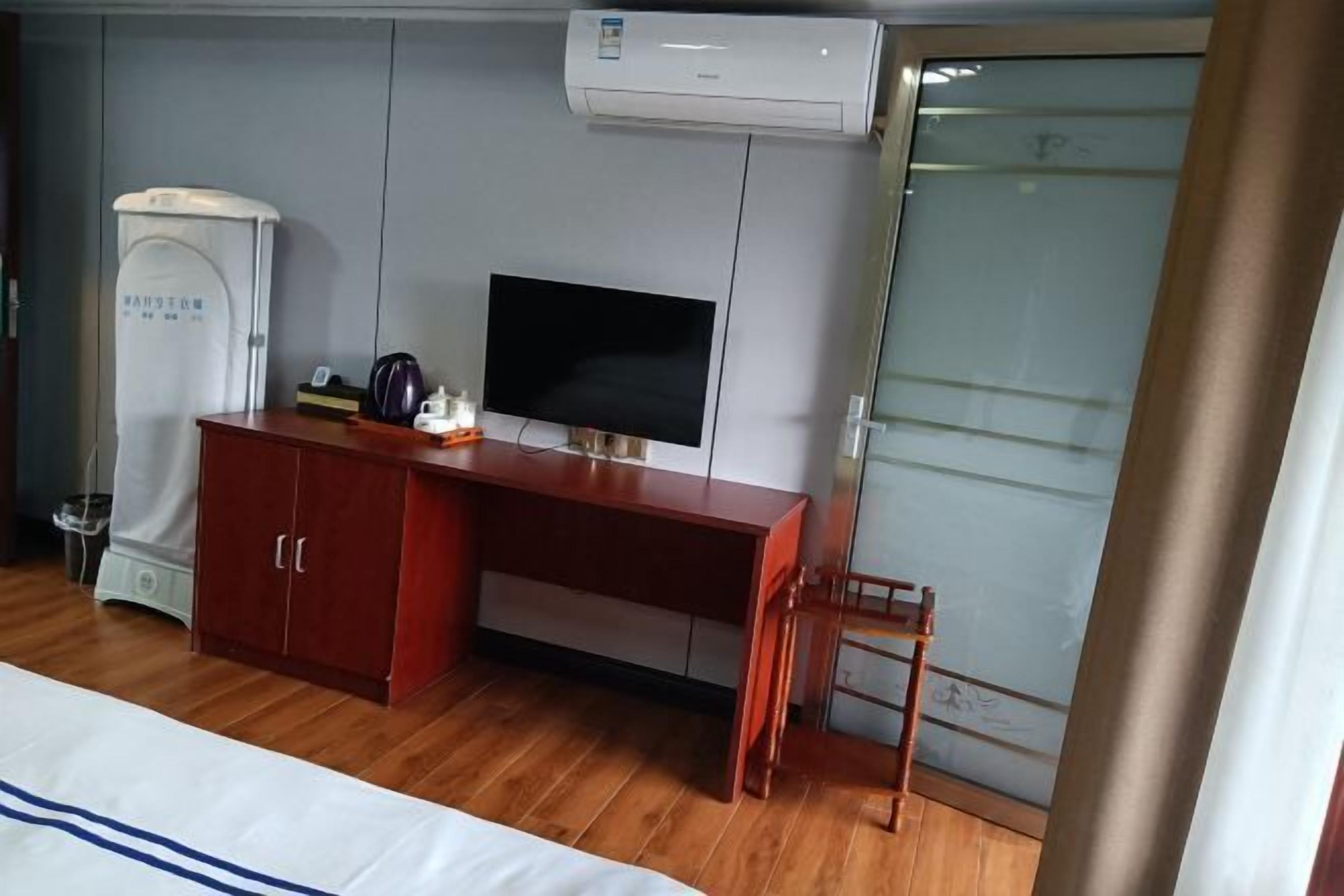 Una habitación de hotel con un escritorio de madera, televisión, armario y baño.