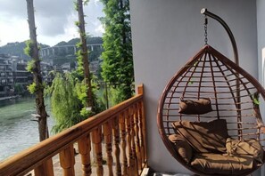 Une balustrade en bois, un fauteuil suspendu avec des coussins et une vue sur une rivière et des bâtiments.