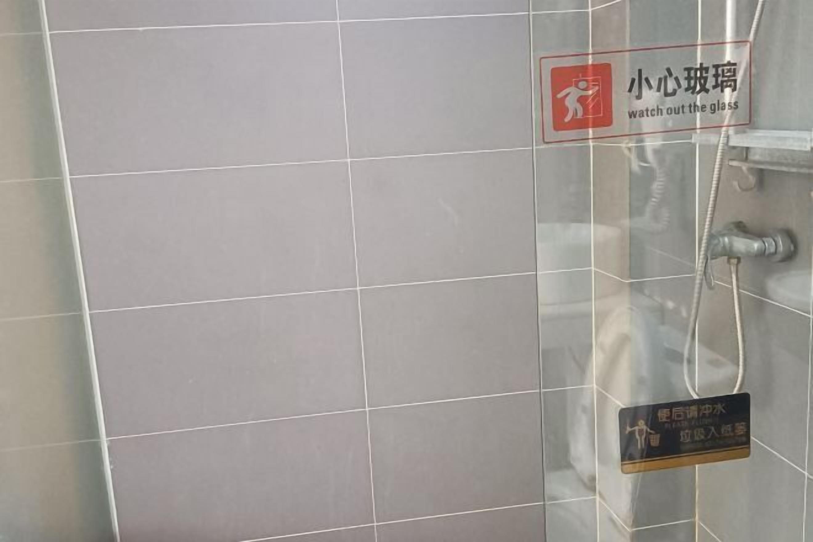 A tiled wall with a sign instructing to watch out for glass.