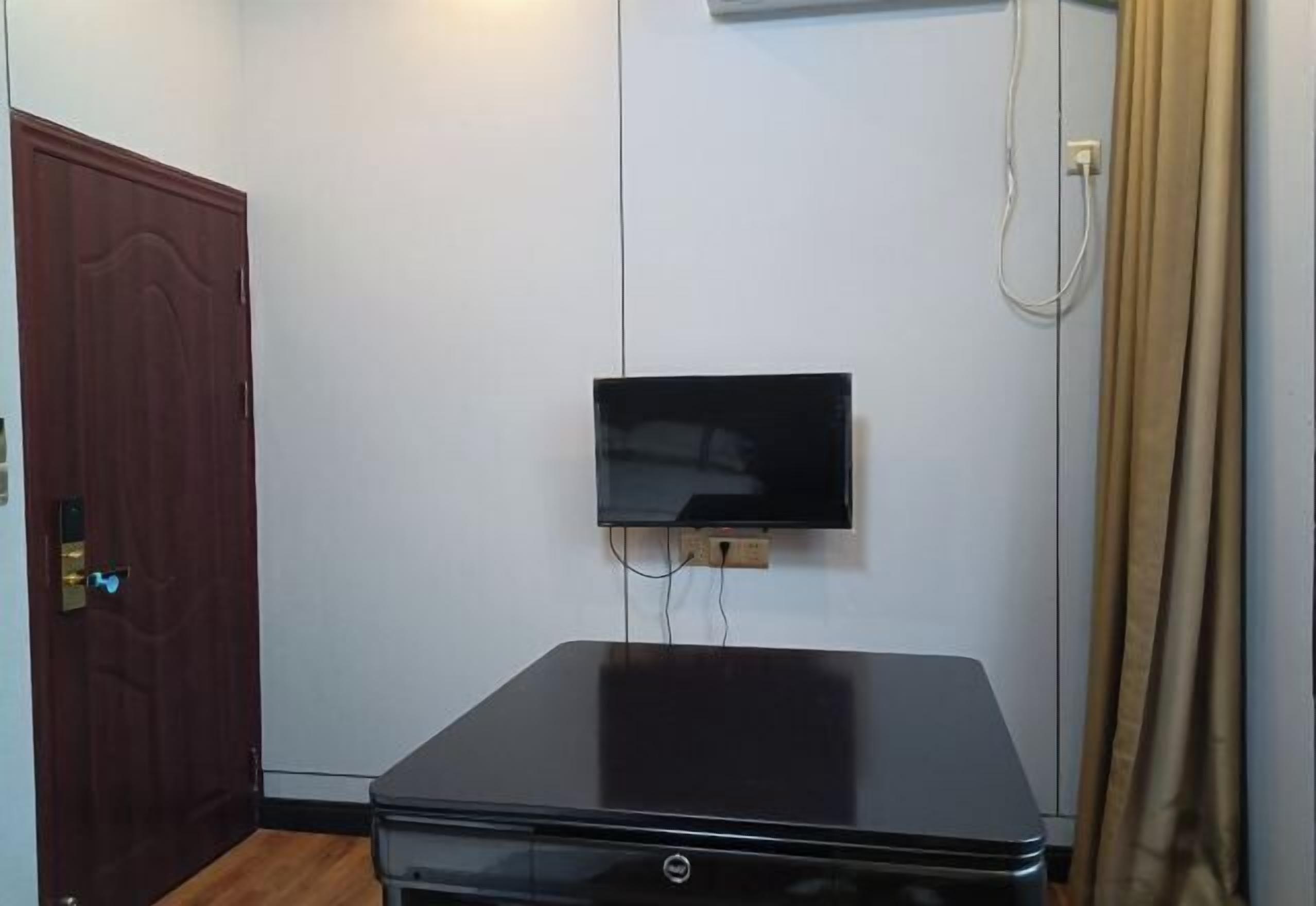 Una habitación con televisión de pantalla plana en la pared, una puerta de madera cerrada y una mesa negra.
