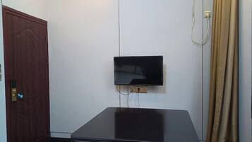 Una habitación con televisión de pantalla plana en la pared, una puerta de madera cerrada y una mesa negra.