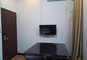 Ein Zimmer mit einem wandmontierten Flachbildfernseher, einer geschlossenen Holztür und einem schwarzen Tisch.