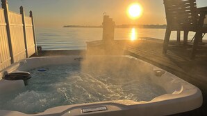 Un jacuzzi con vistas a la puesta de sol sobre el agua, una terraza de madera y una silla.