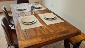 Un comedor con una mesa de madera dispuesta para cuatro, una ventana con vista al mar y un cuadro de veleros en la pared.
