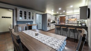 Una cocina moderna con armarios blancos, una isla central con taburetes, una mesa de comedor con sillas y un camino de mesa estampado.