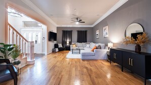 Un salón espacioso con suelo de madera, un sofá gris, un armario negro y una escalera que lleva a otra habitación.