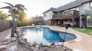 Una piscina residencial con borde curvo, rodeada por un borde de piedrecitas y palmeras.