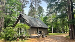 Une cabane avec un toit en pente, une terrasse et entourée d’une forêt dense.