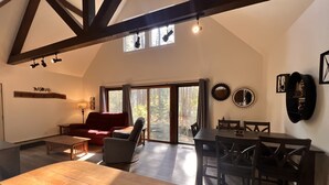 Un vaste espace de vie comprenant une table à manger en bois, un canapé rouge et un fauteuil gris. Une grande fenêtre offre une vue sur l’extérieur.