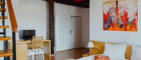 A bedroom with a bed, a desk, a chair, a television, and a painting on the wall.