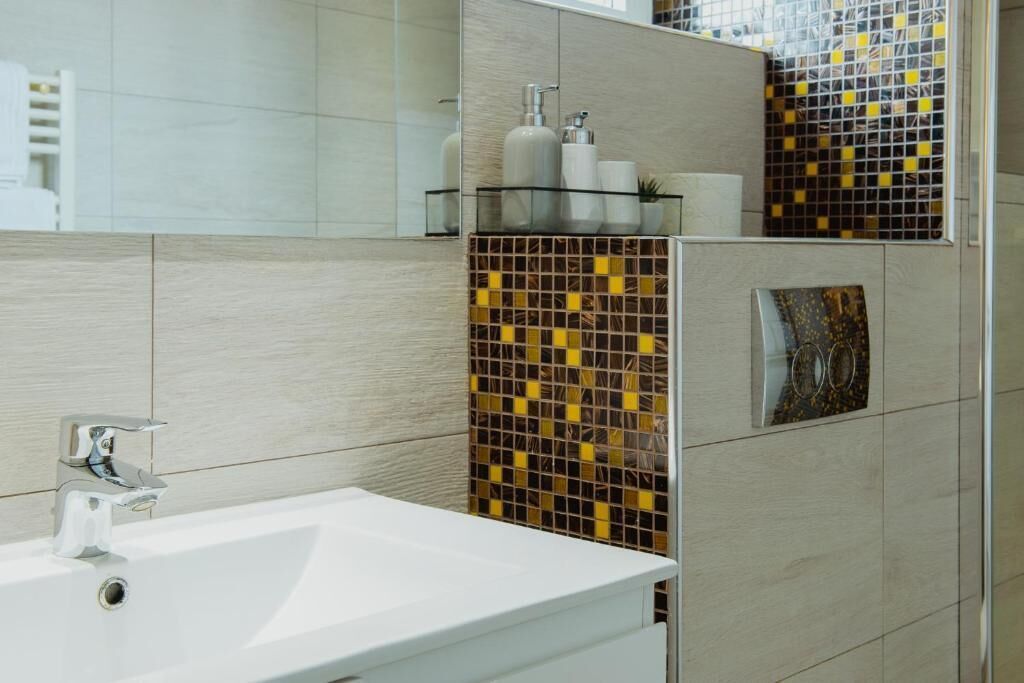 A modern bathroom with a white sink, tiled walls, and a decorative mosaic backsplash.
