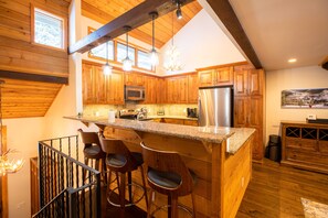 A kitchen with wooden cabinets, a stainless steel refrigerator, a microwave, and a bar area with stools.