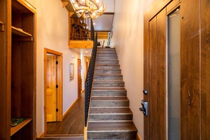 Staircase leads to an upper level, flanked by doors and a chandelier.