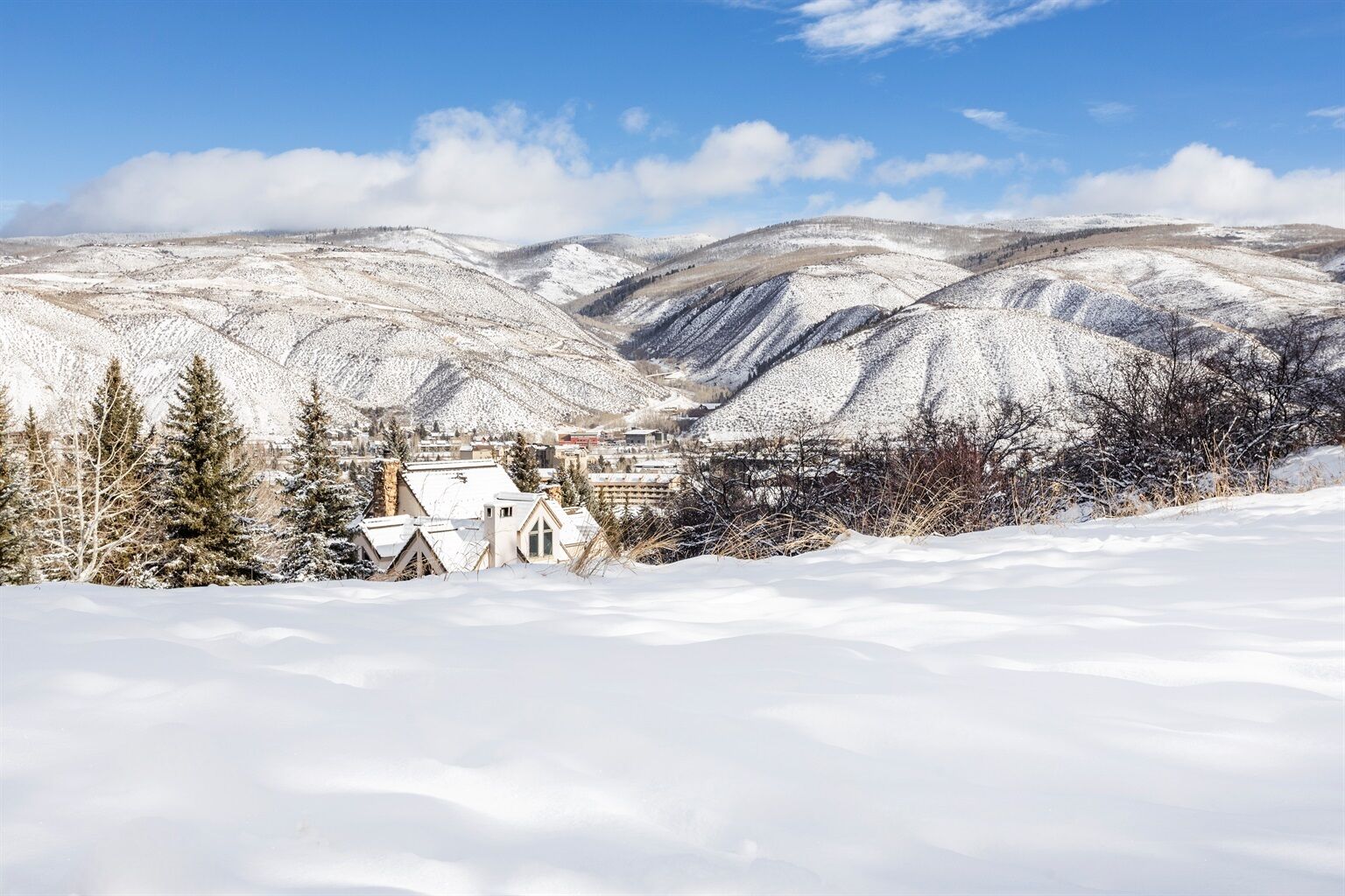 A snow-covered landscape with a town nestled in the valley, featuring traditional buildings and a clear view of the surrounding mountains.