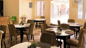 Un espace repas comprenant plusieurs tables rondes et des chaises, un évier et une fenêtre donnant sur l’extérieur.
