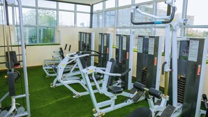 Une salle de sport équipée de divers appareils d’exercice, dotée d’un sol en gazon synthétique et de grandes fenêtres laissant entrer la lumière naturelle.