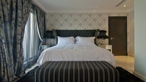 Une chambre à coucher bien aménagée, avec un grand lit, une tête de lit sombre et une table de chevet sur laquelle sont posées deux lampes.