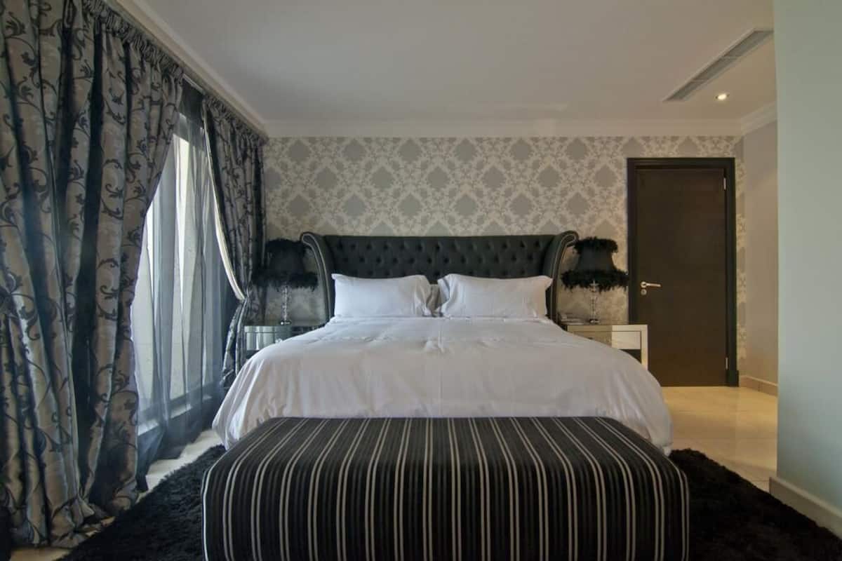 Une chambre à coucher bien aménagée, avec un grand lit, une tête de lit sombre et une table de chevet sur laquelle sont posées deux lampes.