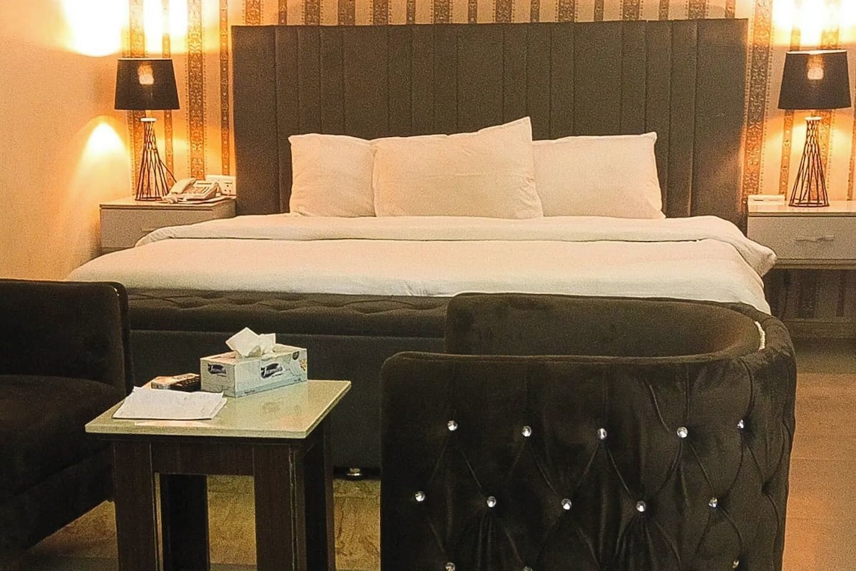 Une chambre d’hôtel avec un grand lit, deux tables de chevet avec des lampes, une petite table avec une boîte de mouchoirs et une chaise.