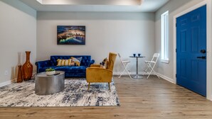 Een woonkamer met een blauwe bank, een gele fauteuil, een salontafel en een schilderij aan de muur.