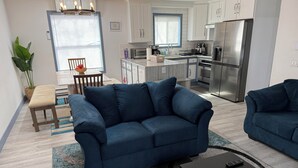 A modern living room with a blue sofa, a coffee table, and a dining area with a wooden table and chairs. - Private Pocono Getaway (Tobyhanna)