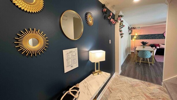 Un couloir aux murs bleu foncé, avec un banc en marbre, un miroir doré et une lampe fixée au mur.